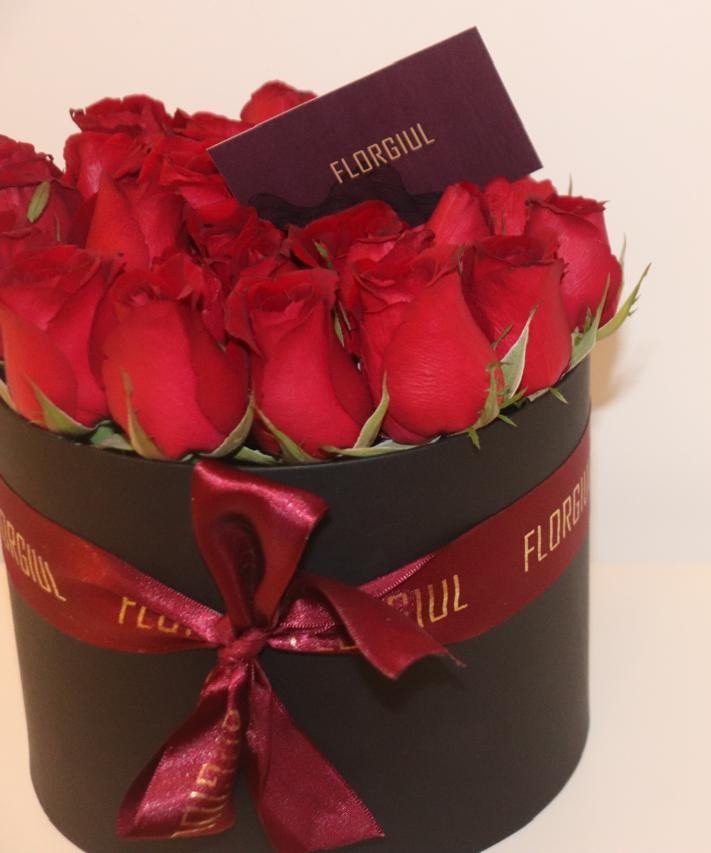 Arranjo floral em caixa redonda preta contendo rosas vermelhas naturais, decorado com fita bordô personalizada da Florgiul e cartão da marca, sobre fundo branco.